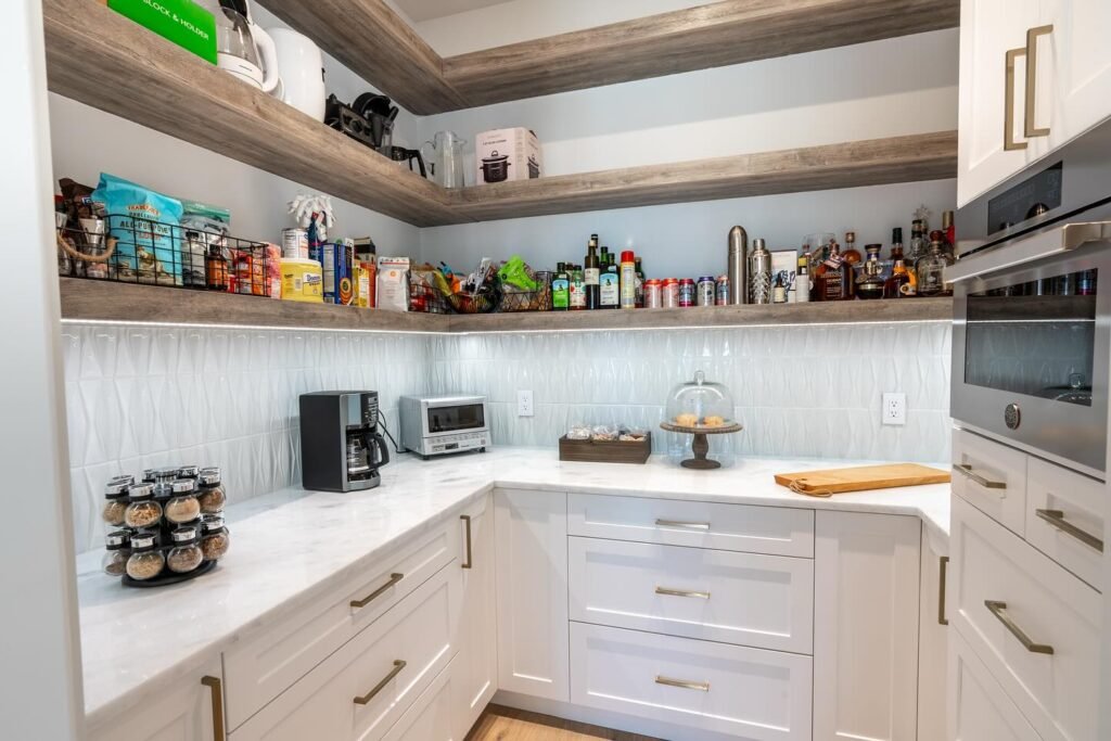 Organized corner pantry with floating rustic wood shelves stocked with spices, bottles, cans, and small appliances, white shaker cabinets, quartz countertop, and textured backsplash in kitchen remodel Salt Lake City
